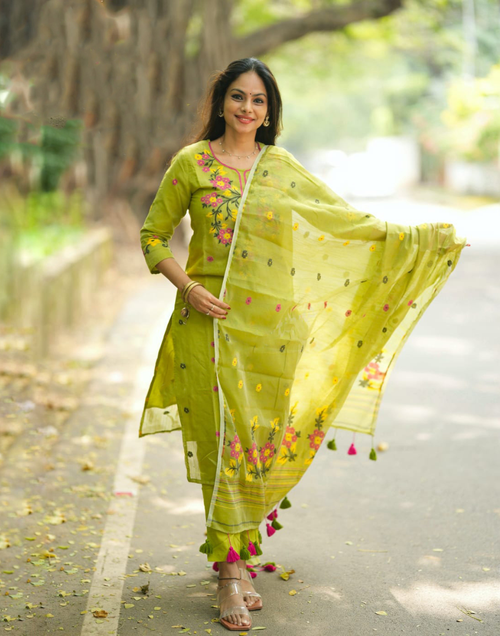 Woman in a green traditional outfit with a floral dupatta standing outdoors.