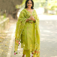 Woman in a green traditional outfit standing on a road with trees in the background