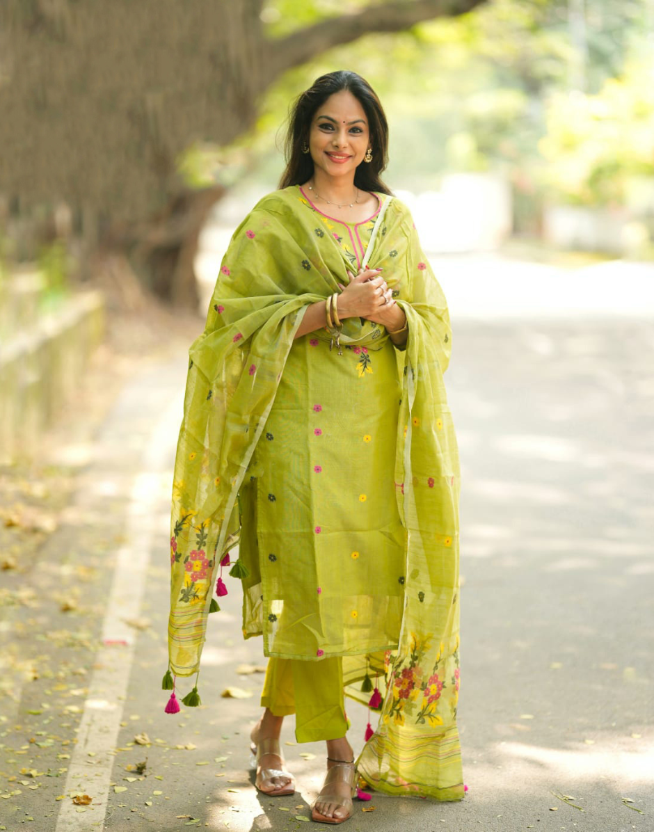 Woman in a green traditional outfit standing on a road with trees in the background