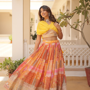 Woman in a yellow top and patterned skirt standing in a decorative outdoor setting.