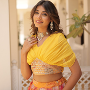 Woman wearing a yellow saree with a floral blouse, standing outdoors.