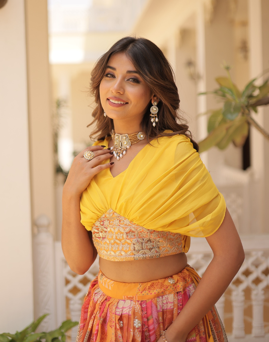 Woman wearing a yellow saree with a floral blouse, standing outdoors.