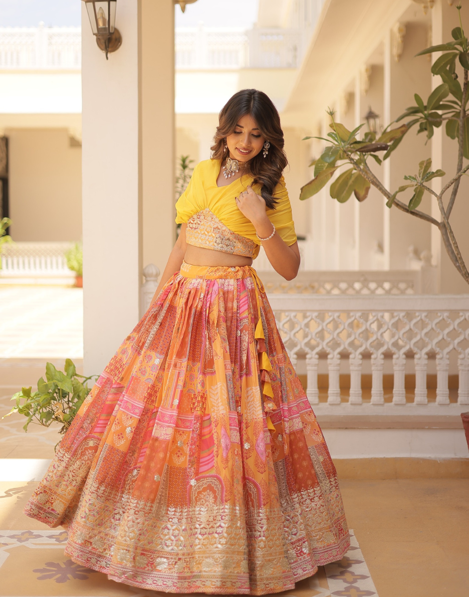 Woman in a yellow top and colorful skirt standing in an outdoor setting with plants and architectural elements.