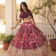 Woman in a traditional outfit with a patterned skirt and purple top, standing in a decorated indoor setting.