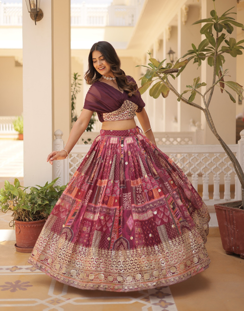 Woman in a traditional outfit with a patterned skirt and purple top, standing in a decorated indoor setting.